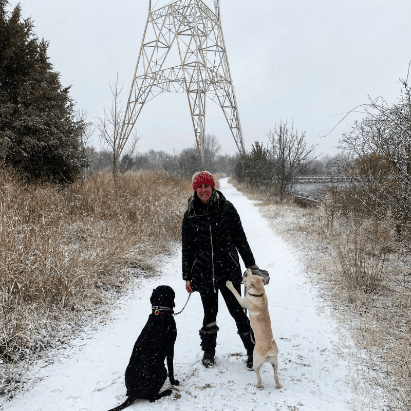 Allison and her pups, Churchill and Cisco, on a snowy path in front of a radio tower.
