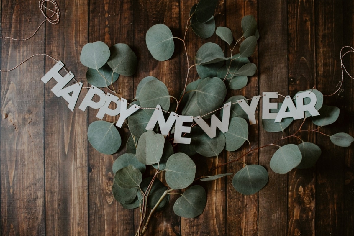 A spray of eucalyptus leaves on a dark wooden table with a garland reading “happy new year”