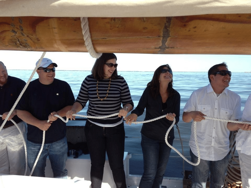 Five people on a boat holding a length of rope and working together.
