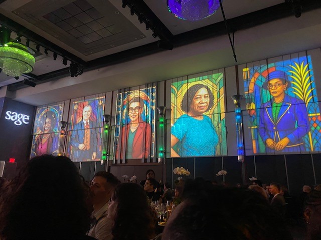 A ballroom with stained-glass portraits of SAGE honorees at their gala. The SAGE logo is visible on the left.