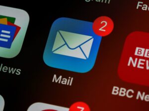 Close-up of a smartphone screen showing the Mail app icon with a red notification badge displaying the number 2, indicating two unread emails. Icons for News and BBC News apps are also partially visible.