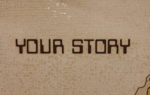 A tiled wall with the words YOUR STORY written in large, bold, black letters on a beige mosaic background.