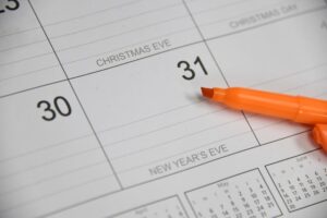 A close-up of a calendar page showing the last days of December, with Christmas Eve on the 24th and New Years Eve on the 31st. An orange marker is placed on top of the calendar.