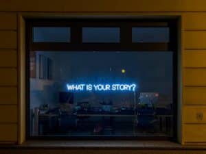 neon sign in office window, with the phrase "What is your story?"