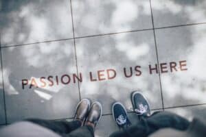 two persons standing on gray tile paving with words "Passion led us here".